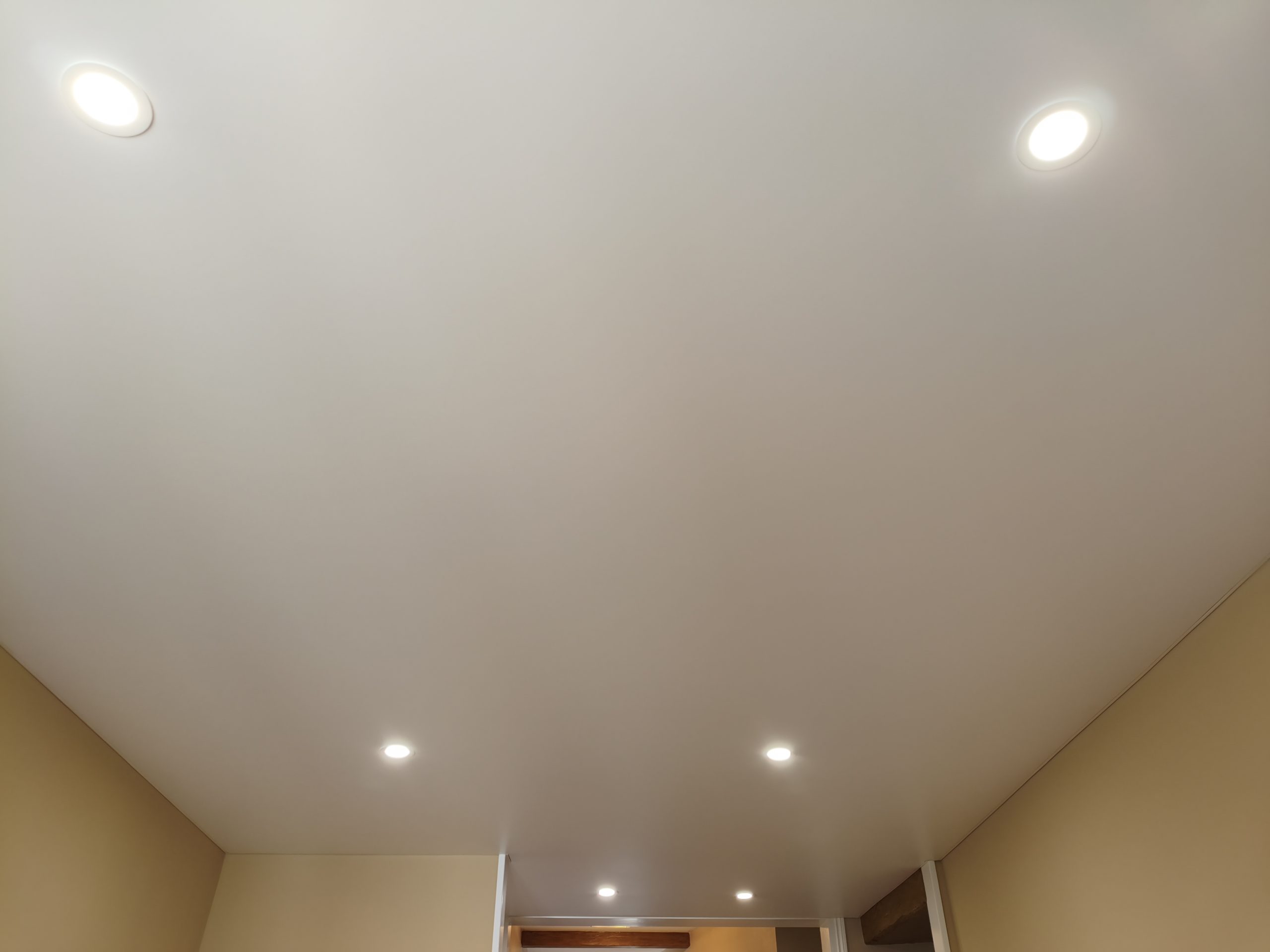 Plafond blanc avec spots encastrés et séparation entre les espaces visible au fond de la pièce.